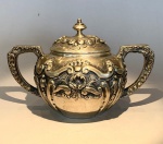 Açucareiro em prata portuguesa  contraste da Águia Açucareiro com tampa, executado em prata portuguesa contrastada (833), compondo conjunto com os lotes anteriores (bules e bandeja). Corpo bojudo com decoração repuxada e cinzelada em volutas e concheados de inspiração rococó, alças laterais simétricas ricamente trabalhadas, tampa destacada com pináculo torneado. Apresenta contraste oficial português com a marca Águia, indicando teor de 833 milésimos, e punções complementares de prateiro e ensaiador (visíveis na base).Peça de grande apuro artesanal, representativa da ourivesaria portuguesa do período final do século XIX. Medidas: 11,5 cm (altura) x 18 cm (largura total) x 12 cm (diâmetro máximo).Material: Prata portuguesa contrastada (833).Peso: 386 gr .Procedência: Acervo família Rezende  residência Av. Atlântica, Copacabana  Rio de Janeiro.