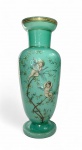 Grande vaso em vidro opalino com decoração esmaltada de putti entre ramagens floridas.Elegante vaso em vidro opalinado na cor verde jade, com delicada decoração policromada e dourada representando putti alados em travessuras entre ramos floridos e insetos. Bordas e base com frisos realçados a ouro. Peça de grande presença visual, típica da produção centro-europeia de fins do século XIX, com afinidade estilística às manufaturas de Boêmia e França (Saint-Louis e Baccarat), no período de transição entre o Romantismo e o Art Nouveau.Medidas: 37,5 cm de altura x 14 cm de diâmetro.Observação: ínfima lasca na base inferior.Nota histórica:A opalina  vidro leitoso, translúcido e finamente colorido  tornou-se um símbolo de luxo burguês entre 1830 e 1900, especialmente em Paris e Murano. Vasos como este, com putti e flores, evocavam o universo mitológico e sentimental tão apreciado nos interiores vitorianos, sendo frequentemente exibidos sobre consoles ou buffets, como emblemas de gosto e prosperidade doméstica. Faz par com o lote anterior.