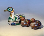ARTE ORIENTAL - Conjunto de três aves em metal esmaltado  técnica cloisonné. China, século XX.Conjunto composto por três pequenas caixas decorativas em formato de patos, confeccionadas em metal com esmaltagem cloisonné policromada sobre base de bronze. Os exemplares apresentam corpo ornamentado por motivos florais e fitomórficos, fundo turquesa no interior e detalhes em azul, vermelho, amarelo, verde e branco.A peça maior possui tampa destacável e dimensões de 11 cm de comprimento x 8 cm de altura. As duas menores, também com tampa destacável têm formato semelhante, medem 6 cm de comprimento x 4,5 cm de altura cada.Em bom estado geral de conservação, com desgaste natural e leve oxidação nos contornos metálicos.Nota técnica:A técnica cloisonné (jingtailan ) consiste na aplicação de esmaltes vítreos coloridos em células delimitadas por finos fios metálicos, que após múltiplas queimas e polimentos adquirem o brilho translúcido característico. Muito apreciada desde o reinado de Xuande (Dinastia Ming, séc. XV), manteve-se viva até o século XX, tornando-se símbolo da arte decorativa chinesa aplicada a objetos de prestígio e coleção