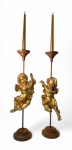 Par de castiçais decorativos com anjos musicistas. Peças aparentemente confeccionadas em Madeira leve (provavelmente pinho de reflorestamento) ou material similar entalhado e dourado a folha de ouro, apresentando figuras de anjos músicos barroquizantes  um portando alaúde e outro flauta  sustentados em hastes metálicas com base circular escalonada em madeira torneada. Estrutura concebida para uma vela cada.Altura total: 50 cm.Velas ilustrativas, não acompanham o lote.