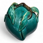 ARTE ORIENTAL - CERÂMICA ESMALTADA. Pêssego em cerâmica esmaltada verde craquelêChina (ou produção oriental inspirada), meados do século XXModelagem orgânica de fruto com folhas aplicadas e ramo em relevo, vidrado em tom esmeralda-esverdeado com craquelê pronunciado. Apresenta pequeno escudo em reserva bege com caracteres incisos em chinês.Altura: 10 cm; diâmetro: 10 cm.Peça sem perdas. Nota do editor:Na cultura chinesa, o pêssego é um dos mais antigos símbolos de longevidade, imortalidade e prosperidade.Segundo a mitologia, os Pêssegos da Imortalidade crescem no pomar da deusa Xi Wangmu (Rainha-Mãe do Oeste) e florescem apenas a cada três mil anos; quem deles se alimenta obtém vida longa e abundante. Por isso, o motivo do pêssego aparece constantemente em porcelanas, bronzes, tecidos e pinturas associados a votos de saúde e fortuna.O vidrado verde-esmeralda não é casual: ele reforça a ideia de vitalidade, renovação e energia primaveril  atributos que, na estética oriental, ligam-se à madeira e ao despertar da natureza. O craquelê é intencional, evocando a textura de antigas cerâmicas Song (séculos XXIII).O selo em relevo apresenta ideogramas que correspondem, muito provavelmente, a Dong Yu, expressão usada em oficinas chinesas e japonesas do século XX para designar jade do oriente ou joia oriental. Trata-se de marca comercial genérica, não de um artista. O uso do termo remete à tradição de comparar o esmalte verde translúcido ao brilho do jade.