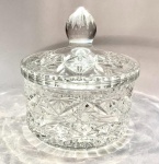 Bombonière em cristal moldado e lapidadoEuropa Central (possivelmente Tchecoslováquia), séc. XX (meados)Peça em cristal transparente, corpo cilíndrico com decoração em estrelas e losangos lapidados, tampa com pega em forma de gota facetada e fundo com estrela radial em relevo.Medidas: 18 cm de altura x 15,5 cm de diâmetro.Leitura: típica produção centro-europeia do pós-guerra, de inspiração boêmia, evidenciando o domínio técnico da lapidação manual e o equilíbrio entre funcionalidade e ornamentação.Condição: excelente, sem bicados aparentes.