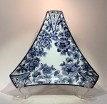 Covilhete triangular  Real DArte Portugal, Tina Salgado. Porcelana portuguesa de corpo fino e esmalte branco de alto brilho, em formato triangular de bordas elevadas.Decoração manual em tons de azul-cobalto sob o vidrado, com motivos florais estilizados distribuídos em padrão contínuo de inspiração orientalista.Assinatura manuscrita da artista Tina Salgado e marca da fábrica Real DArte  Portugal no reverso, acompanhadas da inscrição Hand painted.Medidas: 28 x 28 x 28 cm.Exemplar contemporâneo de fino acabamento, em que a pintura livre e fluida traduz o diálogo entre a tradição decorativa portuguesa e o repertório oriental do azul sobre branco  herança direta das porcelanas de exportação dos séculos XVII e XVIII reinterpretadas sob estética moderna.Condição: perfeita.