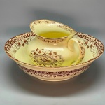 FAIANÇA - Antiga jarra e bacia em faiança em tom bege, decorada com folhas de parreira, comcha e arabescos. Med. 15x24x19 cm e 10x34 cm. Fios de cabelo na jarra.