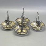 METAL - Conjunto de 4 cestinhos em metal espessurados a prata, interior com resquícios de vermeil, vidro incolor, alça rematada com laço. Med. 12x10x8 cm.