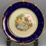 PORCELANA - Prato decorativo em porcelana LINDOLIT decorada com cena central galante policromado, faixa em azul cobalto e detalhes dourados. Dia. 28 cm.