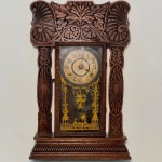 RELÓGIO - Relógio de parede da marca "Ansonia". Caixa em madeira nobre entalhada. Vidro da porta em pintura jateada. E.U.A. Med. 58x37x13 cm. Pêndulo decorado em relevo, representando castelo. Não testado e sem garantia.