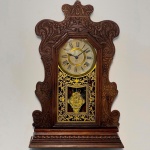 RELÓGIO - Relógio de parede da marca "Ansonia". Caixa em madeira nobre entalhada. Vidro da porta em pintura jateada. E.U.A. Med. 57x38x13 cm. Pêndulo e chave. Não testado e sem garantia.