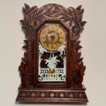 RELÓGIO - Relógio de parede da marca "Ansonia". Caixa em madeira nobre entalhada. Vidro da porta em pintura jateada. E.U.A. Med. 52x68x13 cm. Sem chave, ponteiro dos minutos solto. Não testado e sem garantia.