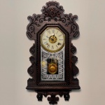 RELÓGIO - Relógio despertador de parede da marca "Ansonia". Caixa em madeira nobre entalhada. Vidro da porta em pintura jateada. E.U.A. Med. 64x33x12 cm. Com chave e pêndulo.  Não testado e sem garantia.