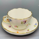 PORCELANA - MEISSEN - Xícara de chá em fina porcelana alemã, na cor branca, decorada com delicadas flores policromadas e frisos dourados. Med. 6x11x9 cm e 14 cm.