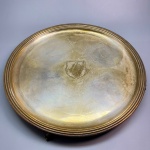 METAL - Linda bandeja redonda, funda lavrada, borda em relevo, elevada por 4 pés. Med. 4x33 cm.
