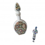 COLECIONISMO - Garrafa em porcelana policromada sobre fundo branco by Veracruz e uma tampa para garrafa em metal e vidro, Alt. 28 e 11 cm.