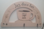Enfeite de parede em tom bege, com a frase Lar doce lar e o desenho de uma xícara com o texto Depois do café eu me expresso. Possui três ganchos para pendurar objetos e detalhes decorativos de grãos e ramos de café. - Medidas: