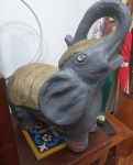 A peça é uma escultura de elefante robusta e pesada, de acabamento artesanal. O corpo é pintado em tom cinza escuro, com detalhes dourados no dorso e na cabeça, além de ornamentos brilhantes que simulam pedras incrustadas nos olhos e nas patas, conferindo um toque decorativo e elegante. O elefante está com a tromba erguida  símbolo tradicional de sorte, prosperidade e proteção. Uma peça marcante, de presença forte, ideal para decoração de interiores ou ambientes temáticos. - Medidas: 32x20x41 cm