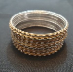 Doze  pulseiras formam um conjunto de braceletes rígidos e finos, em tom dourado, decorados com detalhes prateados em relevo que percorrem toda a circunferência. O contraste entre o dourado fosco e o brilho prateado cria um efeito elegante e sofisticado, ideal para compor tanto looks casuais quanto mais festivos.