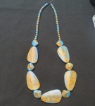 Colar artesanal em resina, com contas esféricas menores em azul e dourado e peças centrais grandes em formato irregular, mesclando tons turquesa e dourado marmorizado. Estilo étnico e contemporâneo, chamativo e elegante