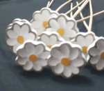 Conjunto com 10 unidades. Enfeites em formato de margaridas feitas em madeira, com pétalas brancas, miolo amarelo e bordas suavemente realçadas em tom mais escuro. Cada flor é fixada em um palito de madeira, ideal para uso como topper decorativo em doces, bolos, arranjos ou outros artesanatos. Peças delicadas e com acabamento artesanal.Altura: 40 cm.