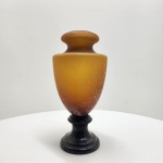 Vaso em pasta de vidro âmbar  Europa, meados do século XX. Elegante vaso inteiramente executado em pasta de vidro (pâte de verre), com coloração âmbar em degradê e textura acidada. A base, igualmente em vidro, forma conjunto harmônico de proporções equilibradas e brilho difuso característico dessa técnica. Obra de grande presença decorativa, representando o refinamento da tradição europeia em vidro artístico. Dimensões: 37 x 18 centímetros.