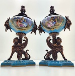 Par de urnas em porcelana Sèvres, França, séc. XIX. Magnífico par de urnas em porcelana francesa Sèvres, ricamente esmaltadas no característico tom bleu céleste, com reservas ovais pintadas à mão representando cenas galantes ao gosto rococó, finamente realçadas por filetes e ornatos dourados. As peças repousam sobre elegantes montagens em bronze dourado com figuras de esfinges aladas, trabalhadas com notável detalhamento. Tampas encimadas por pináculos decorativos. Dimensões: 27 x 13 centímetros.