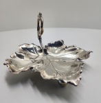 Prato em prata de lei em forma de folha, Peça de prata portuguesa modelada em formato de folha com recortes sinuosos e pegador curvo em espiral, ornado com pequenos relevos naturalistas. Sustentada por três pés esféricos, apresenta excelente acabamento artesanal e brilho característico da prata de lei. O punção visível na haste. A forma e o estilo remetem ao gosto naturalista e decorativo da ourivesaria do período entre 1900 e 1930, comum em pequenas bandejas e peças de apoio de mesa produzidas em oficinas portuguesas. Dimensões:12 x 22 centímetros, Peso: 231 gramas.