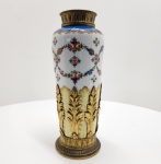 Manufatura de Sèvres  Vaso em porcelana com montures em bronze dourado, França, fim do século XIX. Magnífico vaso em porcelana da Manufatura de Sèvres, ricamente decorado com guirlandas de flores policromadas e rosetas sobre fundo branco, ladeadas por frisos dourados e faixa superior em esmalte azul-cobalto (bleu céleste) com delicados motivos a ouro. A base e o colo são realçados por montures em bronze dourado finamente cinzelado, com ornamentos de folhas de acanto, caneluras e palmetas, características do estilo neoclássico francês inspirado no reinado de Louis XVI. Marcado sob a base com o punção em azul da Manufatura de Sèvres, pintado sob o vidrado, correspondendo ao período de produção do final do século XIX  fase em que a manufatura retomava os temas e acabamentos do século XVIII, preservando a excelência técnica e estética que a consagrou como uma das mais prestigiadas do mundo. Dimensões: 34 x 13 centímetros.