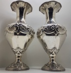 Par monumental de vasos em prata de lei portuguesa 925 estilo Rococó, início do século XX. Com contraste Águia (Portugal, 1º título, 1887 a 1937). Imponente par de vasos em prata portuguesa, com corpo bojudo, pescoço alongado e borda superior recortada em movimento ondulante. As superfícies são profusamente cinzeladas com motivos rocaille, volutas, conchas e folhagens estilizadas em relevo, integradas por frisos perlados e ornatos gravados. A base e o bojo apresentam decoração simétrica e volumetria equilibrada, expressando a estética exuberante do estilo Rococó, da ourivesaria portuguesa. Apresentam o punção oficial português da Águia (1º título), utilizado entre 1887 e 1937, certificando prata de teor 925, acompanhado de contraste de oficina, assegurando origem e autenticidade. Dimensões: 58 x 26 centímetros cada. Peso: 5,458 kilos.