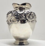 Vaso em prata portuguesa de 1º título (916 milésimos), contraste da Águia  estilo Rococó, início do século XX. Elegante vaso em prata portuguesa contrastada com a marca da Águia, peça de corpo bojudo e pescoço ligeiramente expandido em borda recortada. A superfície é ricamente cinzelada e repuxada com ornamentação de inspiração rocaille, composta por volutas, flores e conchas em alto relevo, entre áreas lisas polidas que destacam o contraste entre brilho e textura. O trabalho revela grande domínio técnico na ourivesaria, evidenciado pelo refinado detalhamento das guirlandas florais e pelos fundos pontilhados (martelé fin)  acabamento típico das oficinas lisboetas e portuenses do início do século XX. Apresenta o punção português Águia voltada à direita (1º título, 916 milésimos), vigente entre 1887 e 1937, garantindo a autenticidade e a pureza da prata. Dimensões: 30 x 22 centímetros. Peso aproximado: 1,755 kilos.