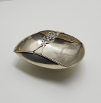 Centro de mesa em prata portuguesa (833 milésimos). Elegante centro de mesa em prata de formato elíptico e bordas suavemente elevadas, o corpo liso e polido é interrompido ao centro por elemento rendilhado em prata vazada, de desenho vegetal estilizado  traço característico da transição entre o Art Nouveau e o Art Déco. A pureza das linhas, aliada ao detalhamento do ornamento central, revela o equilíbrio entre tradição artesanal e modernidade formal. Marcado sob a base com os punções PRATA 833 . Dimensões: 6 x 12 x 9 centímetros. Peso: 108 gramas.