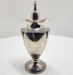 Recipiente para açúcar (Sugar Caddy) em prata portuguesa contrastada com a águia (833).Refinado exemplar de ourivesaria portuguesa, de corpo urniforme facetado e tampa ajustada com pináculo torneado. Apresenta delicada decoração de volutas e flores gravadas, característica das pratas portuguesas da primeira metade do século XX. Peça originalmente destinada à guarda de açúcar ou confeitos, combinando utilidade e sofisticação. Dimensões:27x11centímetros. Peso: 595 gramas.