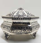 Caixa octogonal em prata ricamente trabalhada, séc. XIX / XX.Peça de ourivesaria de formato octogonal, tampa abaulada articulada e corpo apoiado sobre quatro pés ornados. Toda a superfície apresenta delicado trabalho repuxado e cinzelado com flores, volutas e folhagens, compondo um conjunto de grande riqueza decorativa e equilíbrio formal. De provável produção europeia (possivelmente portuguesa), esta peça representa o refinamento técnico e estético da ourivesaria neobarroca.Dimensões:10 x 15 centímetros. Peso:314 gramas.