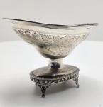 Porta-dragées em prata brasileira, São Paulo, c. 1950.Elegante peça de ourivesaria paulistana, de corpo ovalado gravado com flores e folhagens, borda rendada e base com três pés em volutas. Apresenta contraste do leão coroado e iniciais SP, característicos da prataria paulista de meados do século XX, bem como a marca PRATA 833.Trabalho refinado, representativo da tradição luso-brasileira na produção de prata artística. Dimensões: 11 x 9 x 8 centímetros. Peso:173 gramas.