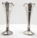 Par de bud vases em prata inglesa, S. L. Bailey  Ltd., Birmingham, 1940Par de bud vases (vasos solitários) em prata de lei (.925), de corpo facetado e forma cônica, apoiados sobre base octogonal e terminados em borda suavemente recortada. Contrastados em Birmingham, com punções da âncora (cidade), leão passante (prata sterling), letra Q (ano 1940) e marca do ourives SLA (S. L. Bailey Ltd.).Modelo de linhas sóbrias e proporcionais, representativo da orfebreria inglesa do período Art Déco tardio, unindo rigor geométrico e elegância contida. Dimensões: 20 x 9 centímetros. Peso: 492 gramas.