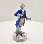 Figura masculina em porcelana Vista Alegre, Portugal, meados do século XX. peça representando cavalheiro do século XVIII, em porcelana moldada e pintada à mão, com trajo típico da época  casaca azul-cobalto, colete dourado com flores e calças listradas em azul e branco. Base rococó ornamentada com flores em relevo e detalhes dourados. Marca sob a base: V.A. Portugal (Vista Alegre).Dimensões: 26 x 9 x 12 centímetros. Estado de conservação: apresenta reparo visível no pescoço, ausência parcial de flores na base e leve desgaste do dourado.