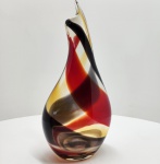 Vaso escultórico em murano artístico soprado, de forma orgânica e torsionada, apresentando composição cromática em vermelho rubi, âmbar e preto fumê, entrelaçados em faixas espiraladas que se fundem no corpo translúcido de base incolor. A obra revela a técnica de sommerso  (vidro sobreposto), característica das oficinas de Murano, onde camadas de vidro colorido são encapsuladas em cristal límpido, produzindo efeitos de profundidade e movimento interno. A espessura generosa do vidro e o brilho impecável do acabamento indicam execução manual de alto nível, com polimento em fogo e modelagem livre, sem o uso de moldes. A silhueta alongada e o ápice levemente curvado conferem à peça uma presença escultórica e dinâmica, típica da produção artística veneziana das décadas de 1950-1970, quando o design em vidro alcançou pleno reconhecimento internacional.Dimensões:42 x 20 x 12 centímetros.