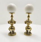 Par de castiçais em bronze dourado, com bases tripartidas de apoio e fustes esculpidos com painéis em relevo. As formas robustas e simétricas, associadas ao acabamento manual, evidenciam um trabalho artesanal de caráter decorativo asiático, possivelmente chinês, executado no início do século XX. Os bobeches circulares mantêm os pinos originais para fixação da vela. Dimensões: 25x5x5 centímetros.
