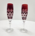 Par de sofisticadas taças em cristal overlay, com camada externa em tom vermelho rubi sobre cristal transparente, lapidadas à mão em padrão de losangos e folhas estilizadas. As hastes facetadas e bases estreladas realçam a pureza e o brilho do cristal, representando com fidelidade a tradição artesanal da cristalaria boêmia. Dimensões:23x6 centímetros.