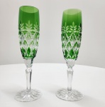 Par de elegantes taças em cristal overlay, com camada externa verde esmeralda sobre cristal incolor, lapidadas à mão em delicado motivo de losangos e folhas estilizadas. As hastes facetadas e bases estreladas evidenciam o brilho e a pureza do cristal, reafirmando o prestígio e a tradição da cristalaria boêmia. Dimensões:23x6 centímetros.