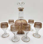 Refinado conjunto de licoreira e seis taças em cristal transparente, ricamente decorados à mão com douração em relevo, apresentando motivos florais e pássaros estilizados de inspiração otomana. A aplicação minuciosa do ouro e o brilho translúcido do cristal evidenciam o trabalho artesanal característico das oficinas turcas do século XX, unindo tradição e sofisticação. Dimensões: garrafa 27x11 centímetros,  taças 11x6 centímetros.