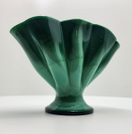 Elegante vaso em vidro artístico soprado, com tonalidade verde intensa mesclada em nuances translúcidas, formando delicado efeito marmorizado semelhante à malaquita. De formato orgânico e ondulado, com abertura em leque e base circular, a peça apresenta proporções equilibradas e brilho vítreo notável. Dimensões:20x26x9 centímetros.