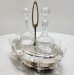 Conjunto de Licor Christofle com Duas Licoreiras em Cristal e Oito Cálices, França, c. 1880 a 1935 Refinado serviço de licor composto por duas licoreiras em cristal lapidado e oito cálices em cristal gravado, apresentados sobre estrutura fixa em metal prateado da prestigiada Maison Christofle. A base traz o tradicional carimbo C  balança  C, utilizado pela manufatura entre o final do século XIX e as primeiras décadas do século XX. As licoreiras, em cristal de grande transparência, possuem tampas facetadas esféricas e decoração gravada em ácido com guirlandas, típica da produção francesa frequentemente associada a fornecedores como Baccarat ou Saint-Louis. Os oito cálices acompanham o mesmo motivo ornamental, formando um conjunto inteiramente coerente e elegante. A estrutura metálica apresenta dois níveis suavemente arqueados para acomodação das taças e espaços centrais destinados às licoreiras, além de alça superior escultural de desenho alongado. Dimensões: 27x27x20 centímetros.