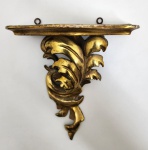 Elegante peanha de parede em madeira entalhada e dourada a folha, de rica ornamentação em volutas e folhas de acanto, típica da tradição decorativa luso-brasileira. A peça apresenta movimentos fluidos e leveza escultural, com pátina original e vestígios do tempo que realçam sua autenticidade e caráter histórico. Inspirada nas formas do Rococó português, esta criação brasileira evidencia a continuidade da arte da talha no país, adaptando o gosto europeu às sensibilidades locais. O resultado é uma peça de sofisticada elegância, ideal para expor imagens sacras, bustos ou pequenos objetos de arte. Dimensões:18 x 17 x 10 centímetros.