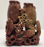 Escultura chinesa talhada em pedra jaspeada, com belíssimo gradiente natural que varia do terracota ao âmbar esverdeado. A peça representa dois vasos baluster unidos sobre base orgânica perfurada, cercados por elaboradas figuras míticas esculpidas em alto-relevo. Na composição frontal, destaca-se o par simbólico Dragão e Fenghuang (Fênix Chinesa)  combinação considerada auspiciosa e associada à harmonia perfeita entre forças masculinas e femininas (Yang e Yin). O dragão, com corpo ondulante, escamas marcadas e cabeça expressiva, aparece em movimento ascendente. A fênix, com plumagem aberta em leque e cauda longa em volutas, surge em postura elegante e protetiva. Dimensões: 22x17x8 centímetros. Apresenta pequenos desgastes e perdas em pontas mais delicadas, comuns em esculturas de pedra.