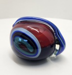 Peça escultórica em vidro maciço, assinada por Molinari, apresentando composição abstrata em massa vermelha com inclusões internas em azul, verde e branco. O movimento ondulante das cores é complementado por uma fita de vidro azul aplicada a quente (glass trailing), criando fluidez e profundidade típicas do design contemporâneo e modelada à mão, com acabamento lustrado e base polida, obra refinada e com cores densas. Dimensões: 12x16x11 centímetros.