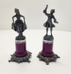 Conjunto composto por duas miniaturas italianas produzidas pela A.C.F em pewter, cada uma montada sobre base de porcelana esmaltada em tom vinho, ornamentada por faixa floral. As figuras representam um casal em trajes do século XVIII, com o cavalheiro erguendo uma taça e a dama segurando seu vestido em pose elegante. As bases em pewter trazem a marca A.C.F  Made in Italy  PELTRO, assegurando origem italiana. Dimensões:13x5x5centimetros.