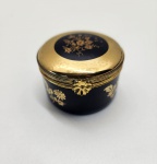 Caixa de porcelana Limoges Castel, marcada e distribuída pela H. Stern, decorada em esmalte azul-cobalto profundo com aplicações de ouro 22k. O corpo e a tampa exibem delicados ramos florais dourados, trabalhados com precisão e brilho impecável. A estrutura metálica apresenta fecho frontal em motivo floral, reforçando o acabamento luxuoso característico das peças produzidas em Limoges para joalherias de prestígio. Interior igualmente esmaltado em azul com detalhe floral pintado a ouro na tampa, demonstrando refinamento em todos os ângulos. Dimensões: 3x5 centímetros.