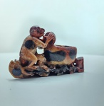 Escultura antiga talhada em pedra jaspeada, representando um macaco ajoelhado diante de um pequeno recipiente ritualístico, em uma postura expressiva que sugere cuidado, observação ou oferenda. A peça utiliza com excelente efeito as variações naturais da pedra  manchas escuras, áreas ocres e tons marmorizados  criando profundidade e contraste visual. O trabalho revela entalhe artesanal de caráter primitivo, com forte linguagem etnográfica asiática, ressaltando o macaco como símbolo de inteligência, astúcia e conexão espiritual. Dimensões: 7x11x3 centímetros.  Apresenta pequenos desgastes e perdas em pontas mais delicadas, comuns em esculturas de pedra.