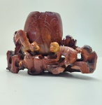 Escultura oriental em pedra dura jaspeada, finamente talhada à mão, representando dois macacos entre rochedos e folhagens, compondo a base de um antigo porta-pincéis ou suporte de estúdio. A peça exibe forte presença decorativa, com nuances naturais da pedra em tons de vermelho-terra, âmbar e inclusões escuras que acentuam o caráter orgânico do material. Os macacos  símbolos tradicionais de inteligência e proteção no repertório asiático  aparecem em movimento, com expressivas feições entalhadas e postura dinâmica. Trabalho de carver experiente, com rica perfuração, volume bem resolvido e pátina antiga que reforça a autenticidade e a idade da peça. Dimensões: 10x14x6 centímetros.  Apresenta pequenos desgastes e perdas em pontas mais delicadas, comuns em esculturas de pedra.