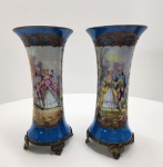 Par de vasos em porcelana SÈVRES, ambos marcados na base, decorados com sena galante pintada à mão e fundo clássico bleu de Sèvres. As reservas ovais apresentam sena galante executada com paleta suave e acabamento minucioso, contornada por rica douração aplicada a pincel. O corpo dos vasos exibe esmalte azul profundo com ornamentação dourada em volutas e arabescos característicos da manufatura. As peças repousam sobre bases em bronze trabalhado, com pés em volutas e acabamento condizente com as montagens francesas tradicionais. Interior das bocas com pintura dourada e motivos florais. Vasos marcados SÈVRES, conjunto de grande elegância e forte presença decorativa. Dimensões:28x14 centímetros. ( um dos vasos está colado).