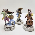 Conjunto de três figuras Capodimonte, peças finamente modeladas em porcelana com músicos de feições caninas em trajes rococó. A pintura é precisa e vibrante, com douração sutil e bases ornamentadas que reforçam a qualidade do trabalho. As poses são equilibradas, os instrumentos bem definidos e o acabamento detalhado confere presença marcante e estética refinada ao conjunto. Dimensões:: 17x17 centímetros cada.